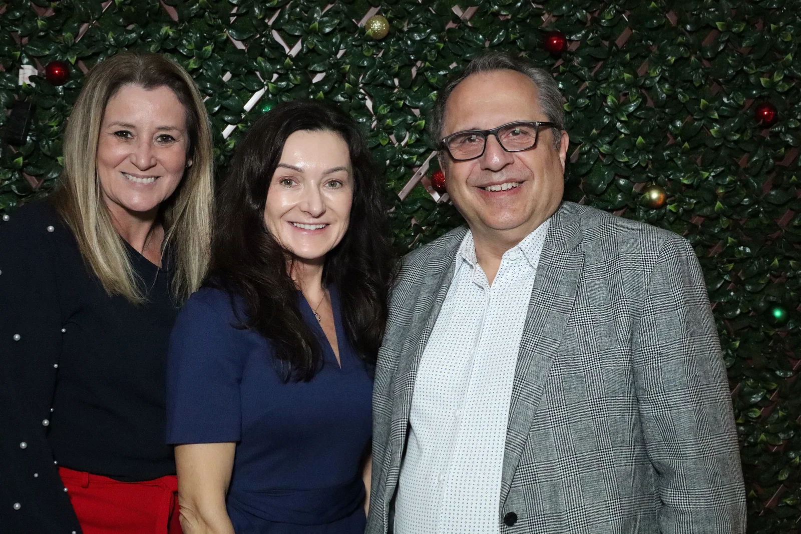 Three KeySmart holiday party guests photographed against a styled greenery wall by Images & Creations